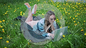Girl lying in the grass, working with a laptop.