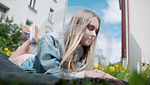 Girl lying in the grass, working with a laptop.