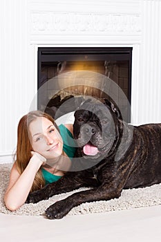 Girl lying near the fireplace with a dog Cane Corso