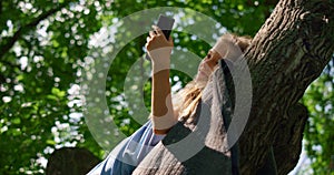 Girl lying with phone on branch close up. Smiling child watching smartphone.