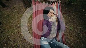 Girl lying with puppies in hammock in autumn park