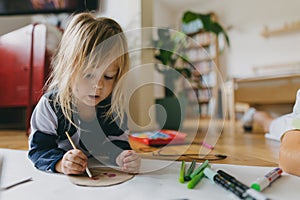 Girl lying on stomach and painting at home with watercolors, markers and tempera paints.