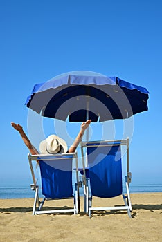 Girl lying on a sun lounger under an umbrella on sandy beach.
