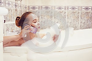 The girl is lying in the whirlpool with foam and talking on a waterproof phone. The girl relaxes and gossips. girl in the foam.