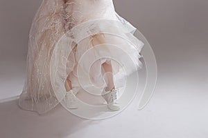 The girl in magnificent wedding dress and white sneakers, legs close-up. Runaway bride