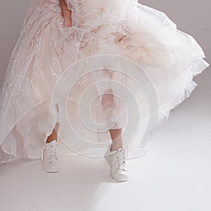 The girl in magnificent wedding dress and white sneakers, legs close-up. Runaway bride