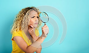 Girl with magnifier lens is distrustful about something. Cyan background