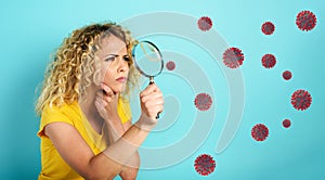 Girl with magnifier lens is distrustful about virus in air. Cyan background