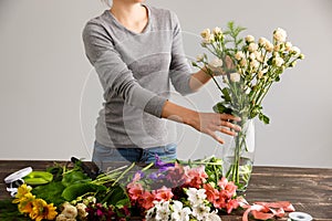 Girl make bouquet over gray background, putting flowers in vase.