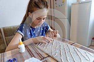 The girl makes crafts, glues cardboard, sits in the home kitchen