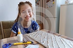 The girl makes crafts, glues cardboard, sits in the home kitchen