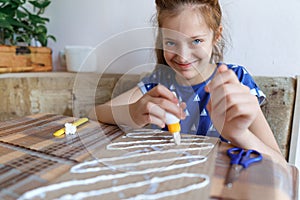 The girl makes crafts, glues cardboard, sits in the home kitchen