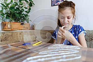 The girl makes crafts, glues cardboard, sits in the home kitchen