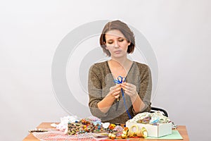 The girl makes a flower of decorative ribbons at the table with needlework