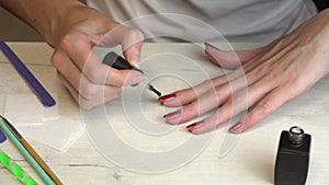 Girl makes herself a manicure and paints her nails with red nail polish with sparkles