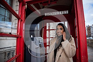 Girl makes a phone call inside a red telephone box in London. Beautiful smiling and attractive woman on the phone