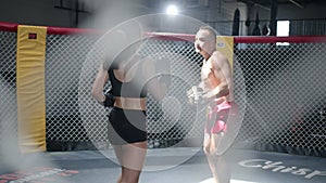 Girl makes punches. Sportive young coach and woman have training in the boxing ring. MMA octagon training.