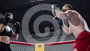Girl makes punches. Sportive young coach and woman have training in the boxing ring. MMA octagon training.