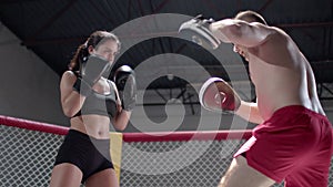 Girl makes punches. Sportive young coach and woman have training in the boxing ring. MMA octagon training.