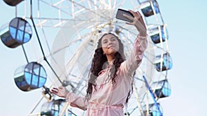 The girl makes selfie using the phone while standing near the Ferris wheel. slow motion