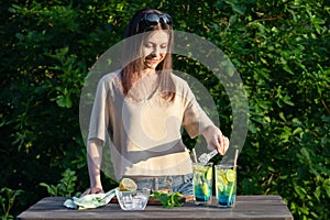 Girl makes summer refreshing cocktails blue lagoon. Process of adding ice cubes to glasses