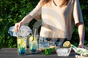 Girl makes summer refreshing cocktails blue lagoon. Process of pouring water into glasses. Selective focus