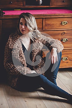 Girl with makeup in coat sitting at floor at home