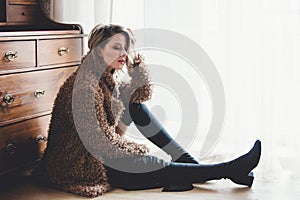 Girl with makeup in coat sitting at floor at home