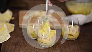The girl making banana pudding in glass glasses in the kitchen. Banana dessert in a glass.