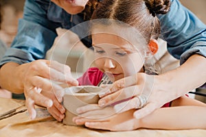 Girl making clay crafts with teacher at table in pottery workshop