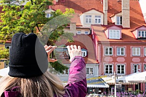 Girl is making photo on her smartphone europian street and houses with orange .tile roof in sunny day,