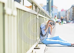Girl making photo with retro camera while sitting on city street