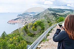 Girl Making pictures from Dubrovnik on the hill with a smart phone in a small road to the Old town in Croatia