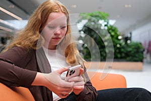 girl in Mall sits using phone to communicate with friends online shopping order on Internet catching Internet games