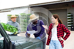 Girl manager discussing with workers delivery of seedlings to farm