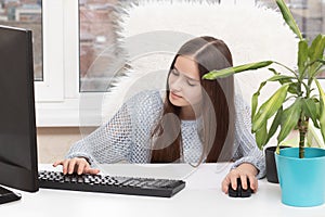 Girl manager in the office of the company is sitting at the table, typing on a computer, smiling