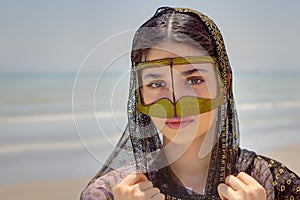 Girl in mask bandari woman, beach of Persian Gulf, Iran.