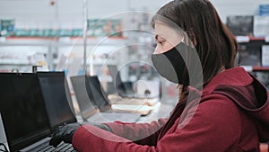 Girl in mask and gloves buys laptop in an electronics shop