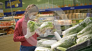 Girl in mask and gloves chooses fresh cabbage vegetables in supermarket, quarantine coronavirus covid-19