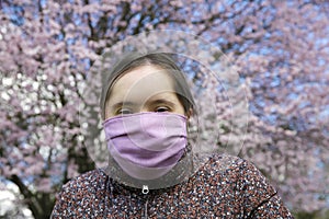 Girl with mask on her face on background on the blooming tree
