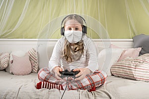 Girl in a mask playing on a game console during quarantine on the bed