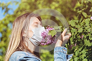 The girl in the mask sniffs a lilac on the street. Concept on quitting quarantine