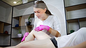 Girl is a master of sugar epilation, holds the model`s leg and evaluates the work