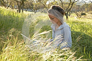 Girl on the meadow relaxing and using a laptop