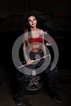 girl mechanic sitting on a tire holding a wrench in his hand. colorless life concept