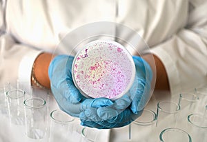 a girl in a medical gown and gloves holds a photo gonorrhea from a microscope in a round frame