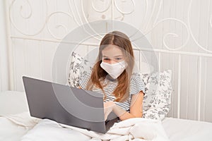 Girl in medical mask in bed studying on laptop. photo