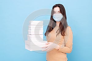 Girl in a medical mask on a blue background with lots of gift boxes. safe delivery. online shopping. space for text