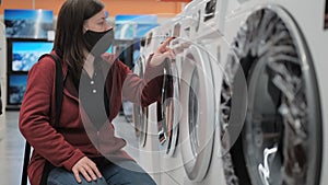 Girl in a medical mask buys a washing machine in a shop