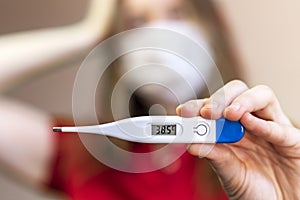 Girl in a medical mask demonstrates an Digital thermometer.